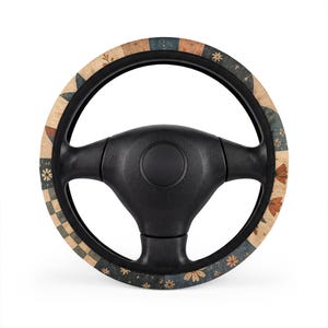 Puede incluir: Un volante negro con una funda circular de diseño patchwork. El patrón consiste en cuadrados alternos en beige, azul oscuro y naranja, decorados con pequeños motivos florales, formas de estrellas y líneas de cuadrícula geométricas.