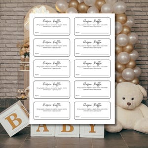 Puede incluir: Una hoja rectangular blanca con diez tarjetas individuales para rifa de pañales con esquinas redondeadas. Cada tarjeta muestra el texto Diaper Raffle, instrucciones para traer un paquete de pañales o toallitas para ganar un premio y una línea.