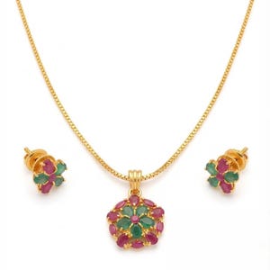 May include: A gold necklace featuring a flower-shaped pendant with oval-cut red and green gemstones, accompanied by a pair of matching stud earrings. Each piece displays a central green stone surrounded by alternating red and green petals.
