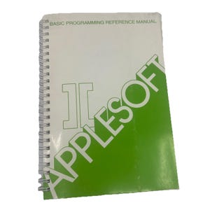 May include: A white and green spiral-bound manual titled BASIC PROGRAMMING REFERENCE MANUAL with the word APPLESOFT printed in large white letters across a green diagonal block and a stylized logo on the front cover of the reference book.