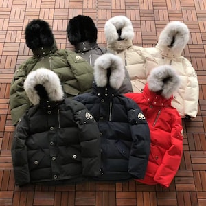 Puede incluir: Una colección de siete chaquetas acolchadas con capuchas ribeteadas en piel, cierres de cremallera frontal y tapetas con botones a presión. Las chaquetas están disponibles en verde oliva, negro, gris, crema y rojo, con un logo metálico.