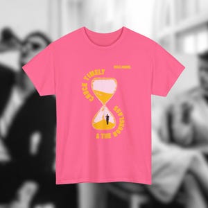 Op de afbeelding: Een felroze T-shirt met korte mouwen en een gele afbeelding van een zandloper met zand erin. De tekst "CHUCK TIMELY & THE HOURGLASS" is in het geel rond de zandloper gedrukt, met "ROLE MODEL" in kleine gele letters erboven.