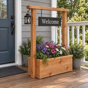 Puede incluir: Una jardinera rectangular de madera con dos postes verticales que sostienen una viga horizontal. Un letrero negro con el texto blanco Welcome cuelga de la viga mediante cadenas. Una linterna negra cuelga del lado izquierdo de la estructura.