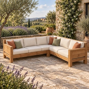 May include: An L-shaped outdoor sectional sofa constructed from light brown wood with thick, cream-colored seat and back cushions. The sofa is accented with several square throw pillows in solid shades of terracotta orange and sage green.