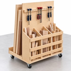 Puede incluir: Un carrito de almacenamiento de madera clara sobre ruedas que cuenta con un panel vertical con seis abrazaderas metálicas fijadas a una barra horizontal, y tres compartimentos frontales llenos de varias tablas, tablones y listones de madera.