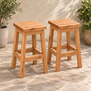 Puede incluir: Dos taburetes cuadrados de madera con un diseño de asiento de listones y cuatro patas rectas conectadas por barras de soporte horizontales en todos los lados. Los taburetes están hechos de madera marrón clara con veta visible y herrajes metálicos.