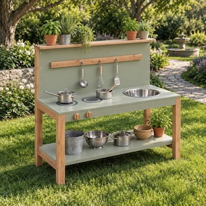 Puede incluir: Una cocina de juguete de madera para exteriores en color verde salvia con fregadero de acero inoxidable, dos quemadores y un estante. Incluye utensilios de cocina colgantes, un cubo de metal, un colador, ollas, cuencos y hierbas en macetas.