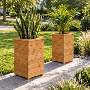 Op de afbeelding: Twee hoge, vierkante plantenbakken gemaakt van horizontale lichtbruine houten latten. Elke plantenbak heeft een eenvoudig ontwerp met strakke lijnen en zichtbare metalen bevestigingen op de hoeken, met daarin een groene plant.