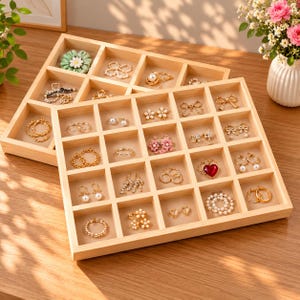 May include: Two light-colored wooden jewelry organizer trays with multiple square compartments. Each section contains various pieces of jewelry, including gold-tone rings, pearl earrings, floral-shaped studs, and heart-shaped charms.