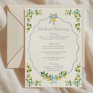 May include: A cream-coloured weekend itinerary card featuring a light blue scalloped border, yellow lemon illustrations with green leaves, and blue ribbon accents. The text details a Friday rehearsal dinner, Saturday wedding events, and Sunday brunch.
