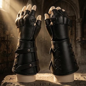 May include: A pair of black fingerless leather gloves featuring reinforced knuckle guards, adjustable straps with metal snaps on one side, and decorative crisscross lacing details on the forearm section, displayed on two mannequin hands.