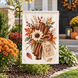 Pode incluir: Uma bandeira de jardim retangular com uma ilustração em aguarela de paus de canela, um girassol branco, bagas vermelhas e folhas de outono. Uma etiqueta bege atada com cordel exibe o texto Cozy Fall com um pequeno coração desenhado.