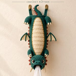 May include: A crochet grocery bag holder shaped like a dark green dragon with a cream-colored belly, red spikes, and small wings. The text reads YarnimalCraft Upside-Down Dragon Grocery Bag Holder CROCHET PATTERN PAGE 1.