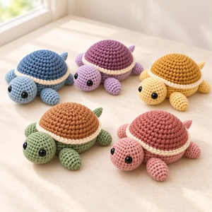 May include: Five small crocheted turtle toys arranged in a group. Each turtle features a textured shell in a different color—blue, purple, yellow, green, and pink—with a cream-colored border, a matching head and limbs, and two black plastic eyes.