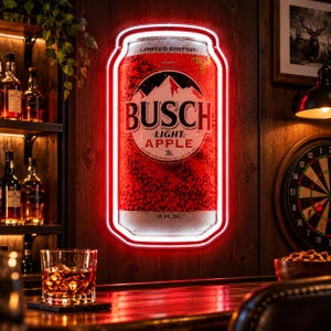 Può includere: Un'insegna al neon a LED rettangolare con la grafica di una lattina di birra rossa Busch Light Apple e il testo Limited Edition, Busch Light Apple e 12 fl. oz. L'insegna è delineata da un bordo al neon rosso vivo su una parete in legno.