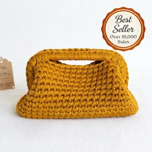 May include: A mustard yellow crochet handbag with a structured frame and integrated handle. The bag features a dense, uniform stitch pattern. A circular badge in the upper right corner displays the text Best Seller Over 10,000 Sales.