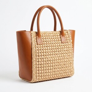 Può includere: Una borsa strutturata caratterizzata da un pannello frontale e posteriore in paglia intrecciata color beige, a contrasto con pannelli laterali in pelle marrone liscia e manici in pelle marrone abbinati. La borsa ha una base rettangolare.