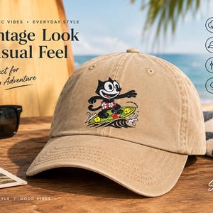 May include: A tan baseball cap featuring a graphic of a black cartoon cat wearing floral shorts while surfing on a yellow surfboard over a wave. The cap has a distressed, washed appearance with a curved brim and a button on the top center.
