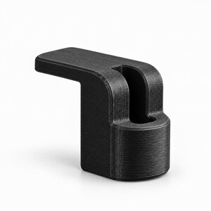 Pode incluir: Um suporte de plástico preto impresso em 3D com uma extensão horizontal plana e uma base cilíndrica vertical com uma ranhura central. A superfície apresenta linhas de camada horizontais finas do processo de fabrico aditivo.