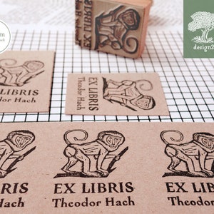 May include: A set of four brown paper cards with black ink stamps of a monkey holding a stick. Each card reads "EX LIBRIS Theodor Hach". The cards are 3x4 cm and are arranged in a grid pattern on a white and black grid background.
