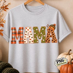 May include: A light gray t-shirt featuring the word MAMA in large block letters. Each letter has a different pattern: red and black plaid, white with small red hearts, green with white flowers, and brown leopard print with a small pumpkin character.