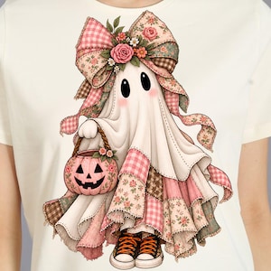 May include: A cream-colored t-shirt featuring a graphic of a white ghost wearing a large pink gingham and floral patterned bow on its head. The ghost holds a pink jack-o'-lantern bucket and wears black and orange lace-up sneakers.