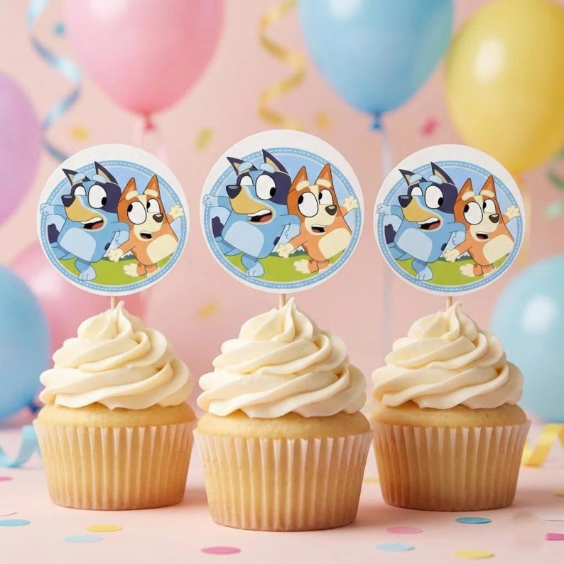 Pode incluir: Tr&ecirc;s cupcakes com cobertura branca, cada um com um topo de papel circular apresentando um c&atilde;o azul e um c&atilde;o laranja. Os topos t&ecirc;m uma borda azul clara e um fundo de grama verde, exibidos contra um fundo de bal&otilde;es coloridos.