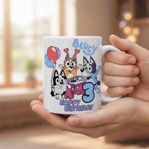Pode incluir: Uma caneca de cer&acirc;mica branca com um gr&aacute;fico colorido das personagens de desenhos animados Bluey e Bingo. O design inclui o texto Bluey, Happy Birthday e um n&uacute;mero 3 grande em azul, juntamente com bal&otilde;es e um piano cor-de-rosa.