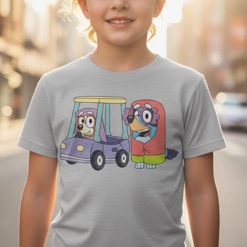 Pode incluir: Uma t-shirt cinza-claro com uma estampa gr&aacute;fica de dois c&atilde;es de desenho animado. Um c&atilde;o conduz um carrinho de golfe roxo com teto amarelo, enquanto o outro c&atilde;o est&aacute; ao lado, vestindo uma pe&ccedil;a vermelha com capuz e detalhes florais rosa.