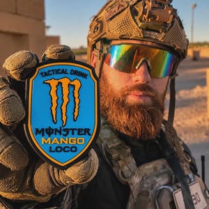 Puede incluir: Un parche con forma de escudo que presenta un fondo azul claro con un borde negro. El texto TACTICAL DRINK aparece en la parte superior, con el logotipo de Monster en amarillo y el texto MONSTER MANGO LOCO en negro y amarillo abajo.