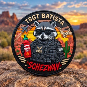 May include: A circular morale patch featuring a raccoon wearing sunglasses and tactical gear, holding a bottle of Sriracha sauce. The text reads TSGT BATISTA, TSGT, 2008, and SCHEZWAN. The design includes a jet, a cactus, and a sunset background.