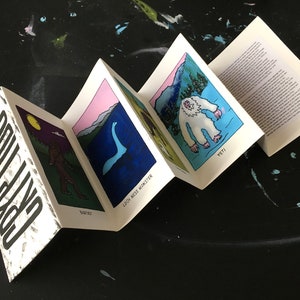May include: A white booklet with the word "Cryptids" printed on the front cover. The booklet is open to reveal illustrations of a Bigfoot, a Loch Ness Monster, and a Yeti.