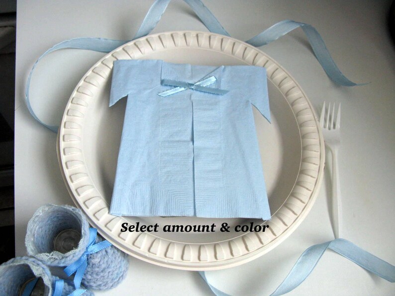 May include: A white paper plate with a blue napkin folded into the shape of a shirt. The napkin has a blue ribbon tied around the neck. The plate is surrounded by blue ribbon.