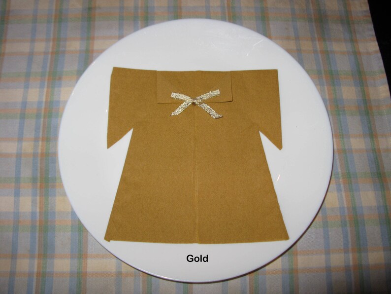 May include: A gold napkin folded into the shape of a dress with a gold ribbon tied around the neck. The napkin is on a white plate with a plaid tablecloth.