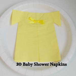 May include: A set of 20 yellow paper napkins folded into the shape of a shirt with a yellow bow. The napkins are on a white plate. 20 Baby Shower Napkins