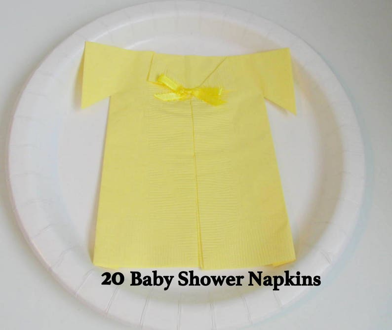 May include: A set of 20 yellow paper napkins folded into the shape of a shirt with a yellow bow. The napkins are on a white plate. 20 Baby Shower Napkins