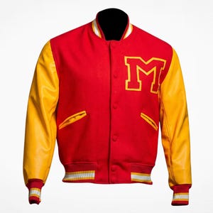 Könnte beinhalten: Eine rote Collegejacke mit gelben Ärmeln und einem großen, gelben Buchstaben M als Aufnäher auf der linken Brustseite. Die Jacke verfügt über eine Druckknopfleiste, zwei Seitentaschen mit gelber Einfassung sowie gerippte Bündchen und einen Saum mit weißen und gelben Streifen.