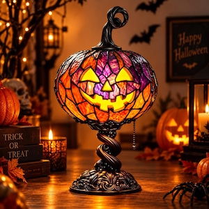 May include: A stained glass jack-o'-lantern lamp featuring orange and purple glass pieces, a black metal twisted stem base, and a pull chain switch. The pumpkin-shaped shade glows from within, displaying a carved face with a wide, jagged grin.