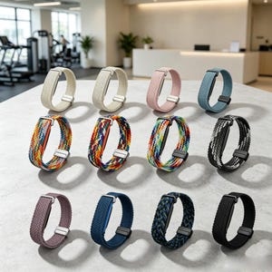 May include: A collection of twelve braided watch bands arranged in three rows. The bands feature various solid colors including beige, pink, blue, and black, alongside multi-colored woven patterns. Each band includes a metallic magnetic clasp.