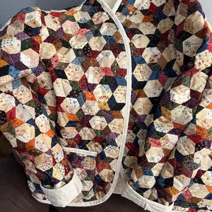 May include: A quilted jacket with a patchwork design. The jacket features a variety of fabric patterns and colors, including red, blue, green, and beige. It has a white trim and a collar.