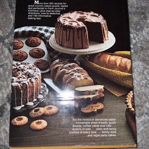 May include: A cookbook cover featuring a variety of baked goods, including a chocolate cake with chocolate frosting, a loaf of bread, and a variety of cookies. The text on the cover reads "More than 350 recipes for great country baked goods, tested and perfected in Farm Journal's Kitchens - plus step-by-step directions, how-to sketches and 150 informative baking tips."