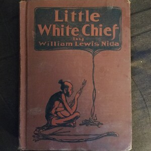 May include: A vintage book titled "Little White Chief" by William Lewis Nida. The cover features a brown background with a black illustration of a Native American person sitting by a fire.