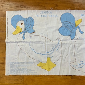 May include: A white fabric panel with instructions for making a Jemima Puddle-Duck stuffed toy. The panel features a line drawing of the duck with a blue bonnet and yellow feet. The text "Jemima Puddle-Duck" is printed in black at the top of the panel.