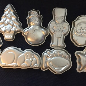May include: A set of nine silver-colored metal cake pans shaped like a Christmas tree, snowman, nutcracker, Santa Claus, a house, a dog, a frog, and a fish.