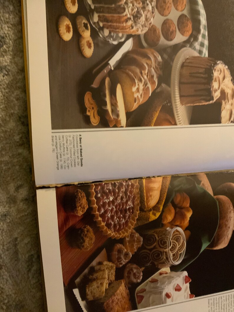 May include: A variety of baked goods, including a coffee cake, muffins, a chocolate cake, a braided loaf, and cookies. The baked goods are arranged on a table with a checkered tablecloth.