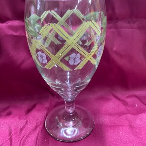 May include: A clear glass goblet with a yellow and green lattice design and purple flowers.