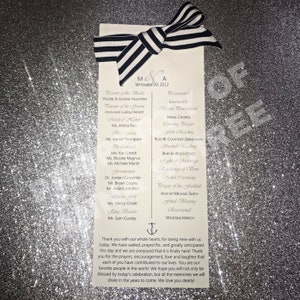 May include: A black and white striped bow sits atop a white wedding program with the names Valerie & George Valentine and the date September 20, 2012. The program lists the order of events for the wedding ceremony, including the bridal chorus, readings, and the wedding march.