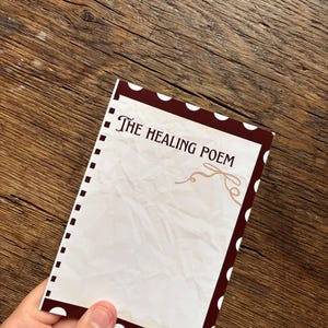 Può includere: Una carta rettangolare con un bordo marrone scuro a pois bianchi. Il centro è color bianco sporco con una texture di carta stropicciata, che mostra il testo "THE HEALING POEM" in un carattere serif marrone scuro e un piccolo ricciolo decorativo.