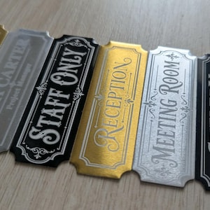 May include: A set of six rectangular metal signs with decorative notched corners. The signs feature various text including Richard Carter Director, Emma Carter Project Manager, Staff Only, Reception, Meeting Room, and Cutlery Kitchen Drawer.