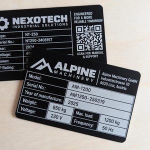 Peut inclure: Deux plaques d'identification rectangulaires en métal noir avec du texte blanc. La plaque supérieure présente la marque Nexotech Industrial Solutions et un QR code. La plaque inférieure affiche les détails Alpine Machinery, incluant le modèle AM-1200, un poids de 850 kg, une tension de 230 V, une charge maximale de 1200 kg et une fréquence de 50 Hz.